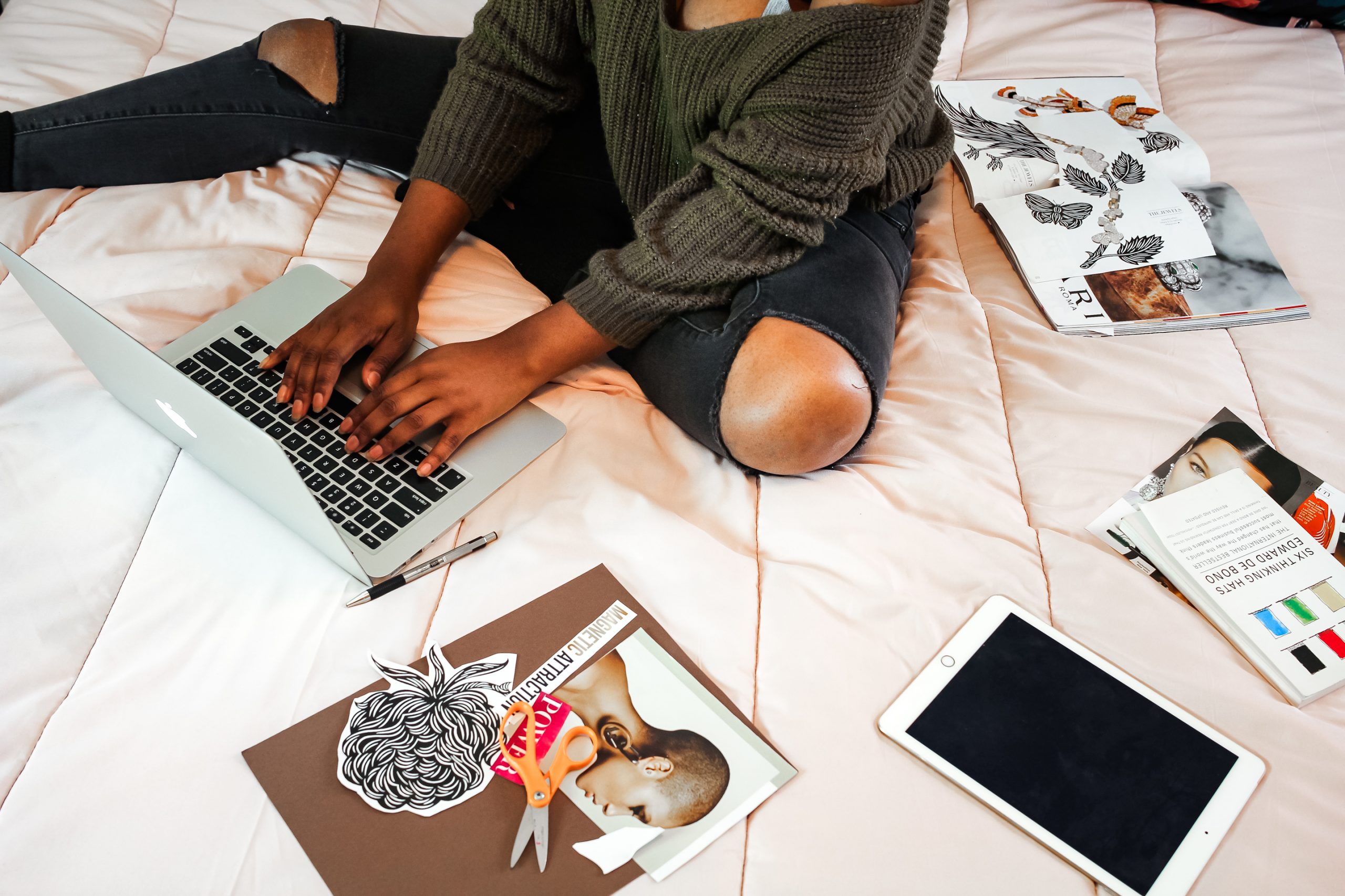 woman on bed surrounded by laptop, magazine clippings, journal and planner - working on a vision board